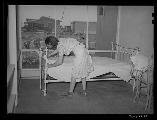 Wife of member of the Casa Grande Valley Farms, Pinal County, Arizona making up bed on her porch. These large porches on all the homes are used for auxillary living quarters