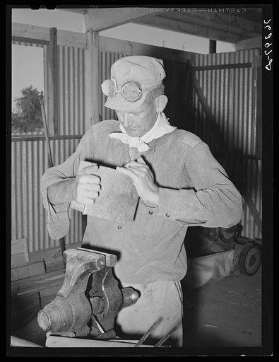 Member of the Casa Grande Valley Farms shaping a piece of tin to repair the hay chopper. Pinal County, Arizona
