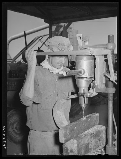 Member of the Casa Grande Valley Farms using an electric drill in making repairs for hay chopper. Pinal County, Arizona