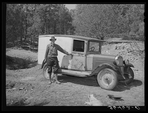 Eugene Davis standing by the side of his adapted truck which carries him about the country on his search for gold. Pinos Altos, New Mexico