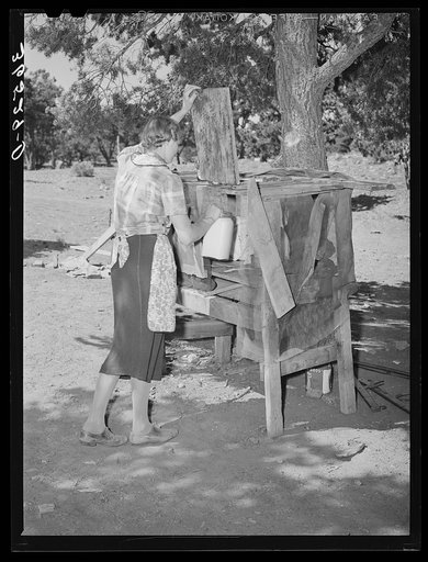 Mrs. Faro Caudill placing milk into homemade cooling box. Damp cloths are wrapped around buckets and jars of milk, and rapid evaporation in the open air produces sufficient cooling to keep milk. Pie Town, New Mexico