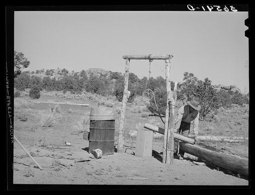 Faro Caudill pouring water from his well into watering trough made of hollowed-out log. Pie Town, New Mexico