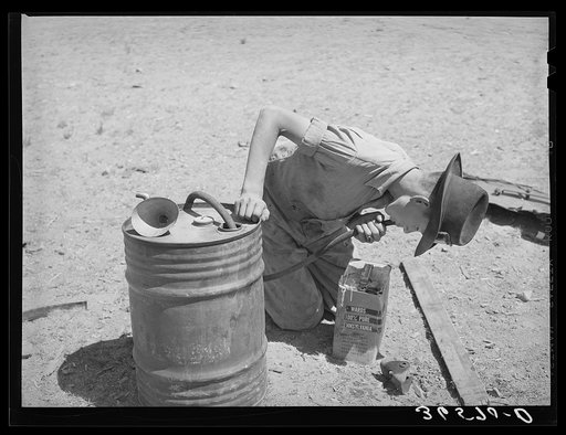 Syphoning gas from storage container to use in truck-tractor. Pie Town, New Mexico