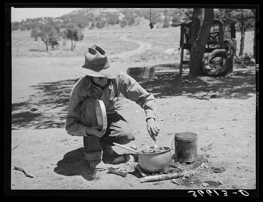 Faro Caudill stirring the stew for dinner. He is cooking over a camp fire because he is engaged in tearing down his dugout and re-building it near his water supply. Pie Town, New Mexico