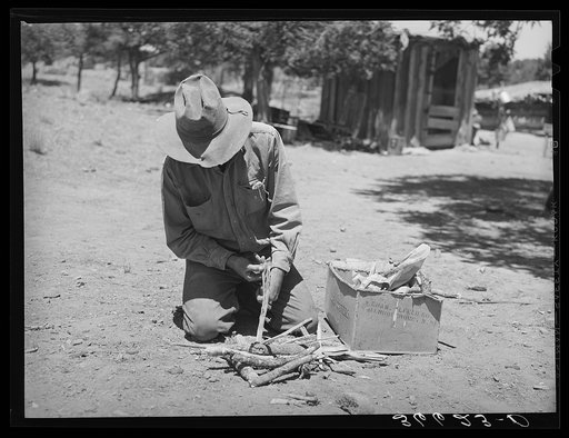 Faro Caudill building a fire to cook dinner while he moves his dugout. Pie Town, New Mexico