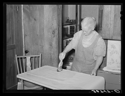 Mrs. George Hutton brushing on paste on wall paper which her son is hanging for her. Pie Town, New Mexico
