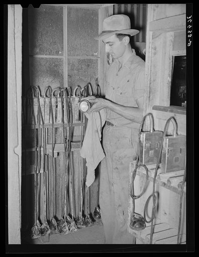Workman checking miners' lights. Batteries of these lights are checked every day. Mogollon, New Mexico