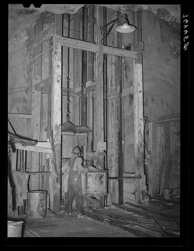 Goldminer pushing car of ore onto hoist. This is elevator to the surface from the 750-feet level. Mogollon, New Mexico
