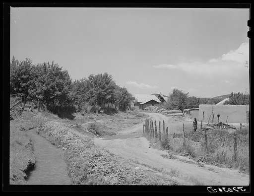 Irrigation ditch flows across road at entrance to Chamisal, New Mexico