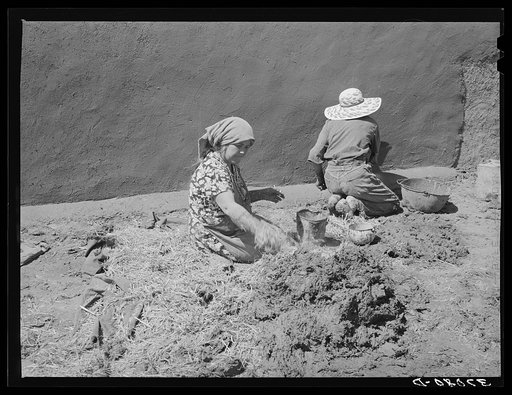 Spanish-American women making plaster of straw and mud to replaster house. Chamisal, New Mexico