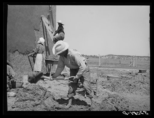 Mixing plaster for house, Chamisal, New Mexico. Occasionally a man helps with the hard work of mixing plaster but the women never allow the men to help with the actual plastering of the house