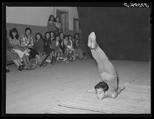 Spanish-American acrobat of traveling show. Audience in background.  Penasco, New Mexico