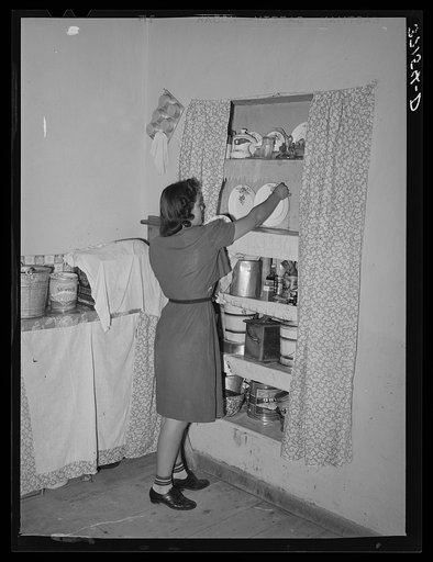 Daughter of Spanish-American putting dishes into cupboard. Chamisal, New Mexico