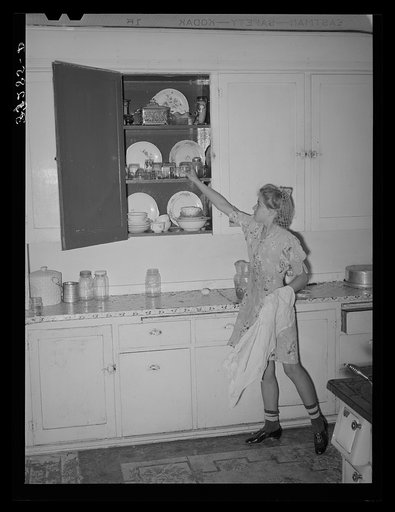 Daughter of Morman [i.e. Mormon] farmer putting away dishes in kitchen cabinet. Box Elder County, Utah