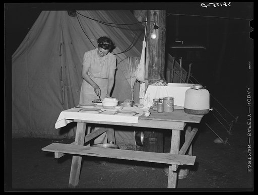 Carpenter's wife setting the table in front of their tent home. Mission Valley, California, which is about three miles from San Diego. These people followed construction work in Texas, Louisiana, Illinois and Arizona. They have never lived in a tent before but the man said, "I know this work-spree i