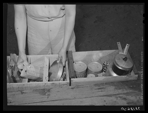 Carpenter's wife unpacking a box of groceries. Mission Valley, California, which is about three miles from San Diego. Flies and smoke from the outdoor fire are their biggest housekeeping problems, she says
