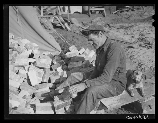 Man who is building a new trailer court scraping secondhand brick which will be used in building a cesspool. San Diego, California. New trailer courts are springing up monthly because they seem to be the preferred type of housing