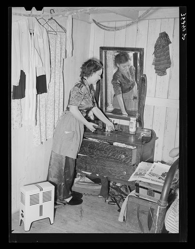 Daughter of carpenter from Hobbs, New Mexico, straightening dresser in room in tourist court which is now the family home