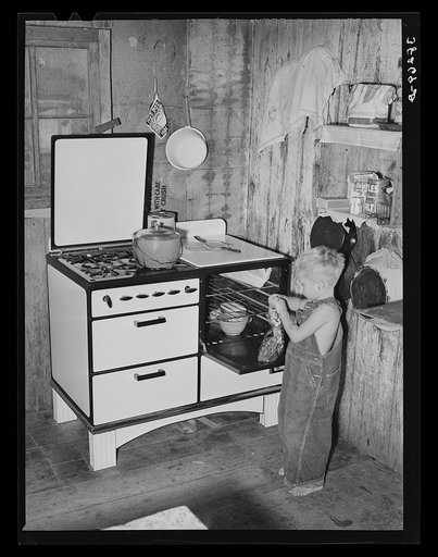 This workman's son is taking gingerbread out of kitchen stove which cost his father one hundred thirty-five dollars and he lives in a shack-house in the Mexican section of town because the father couldn't find anything better for the family. Corpus Christi, Texas