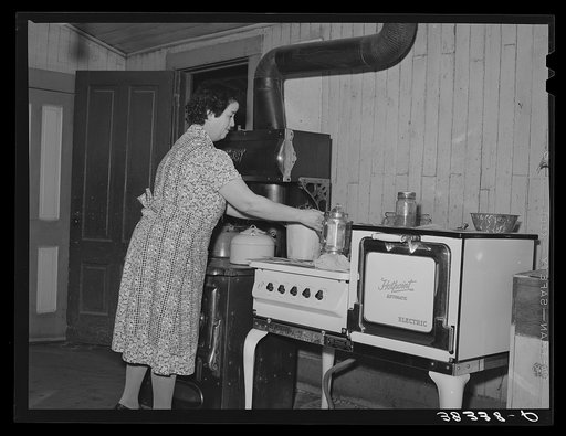 Farmer's wife in her kitchen near Auburn, California. Notice the electric stove and wood or coal range adjoining. This is a common sight in this section which is generally electrified but where electricity rates are higher than many farmers can afford to pay. Placer County, California