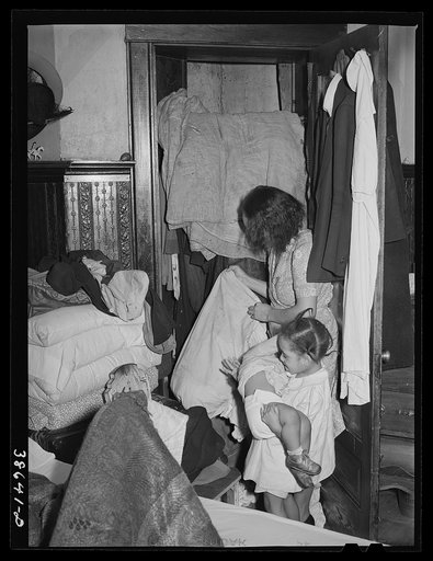 Corner of bedroom with Negro housewife examining bed clothing chewed by rats. Chicago, Illinois
