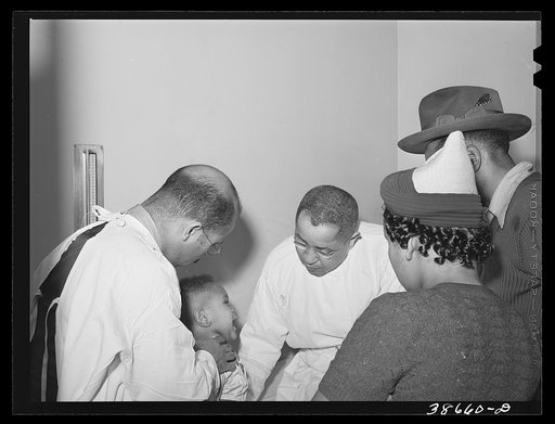 Doctors examining baby whose parents have just brought him into the clinic at the Negro hospital. Chicago, Illinois