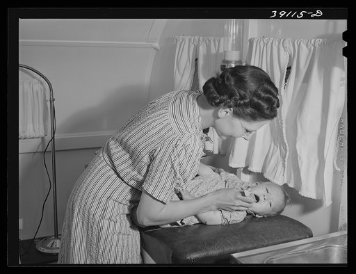 Nurse at the FSA (Farm Security Administration) migratory labor camp mobile unit, examines throat of baby in trailer-clinic. Wilder, Idaho