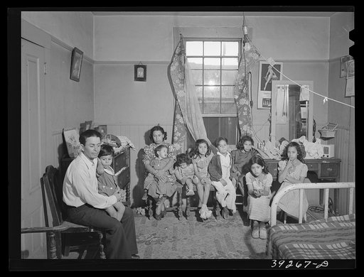 Family group in interior of house in Mexican section. This man is an agricultural worker. This family of two adults and eight children, with another on the way, live in three small rooms, with no bath for which they pay eleven dollars per month. They use an outside toilet shared with five other fami