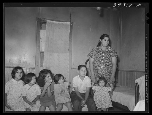 Mexican children with their mother sitting on bed in their home. San Diego, California