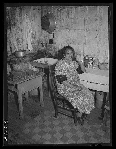 Mexican woman at table in kitchen of her two-room house. San Diego, California