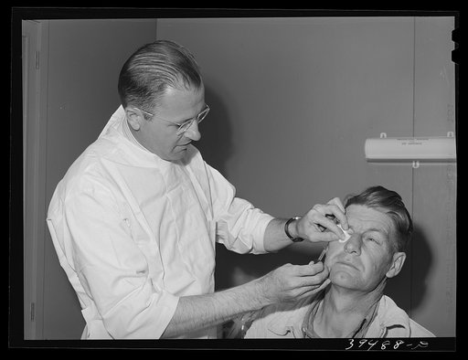 Doctor treats patient's eye (a minor burn) at the clinic at the FSA (Farm Security Administration) labor camp. Caldwell, Idaho. The doctor holds clinic twice a week, a nurse lives at the camp and is always available