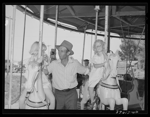 Father with his two daughters on the merry-go-round, one of the carnival attractions at the Fourth of July celebrations
