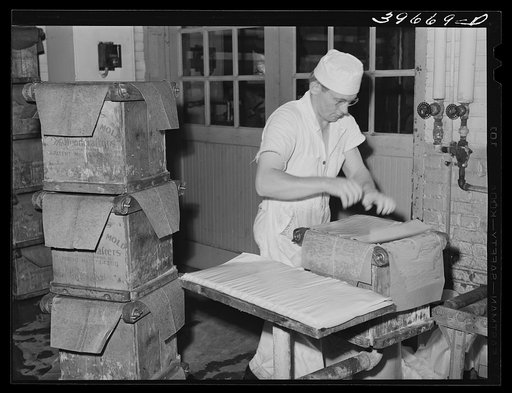 Putting layer of waxed paper over tub of butter at the Dairymen's Cooperative Creamery. Caldwell, Canyon County, Idaho