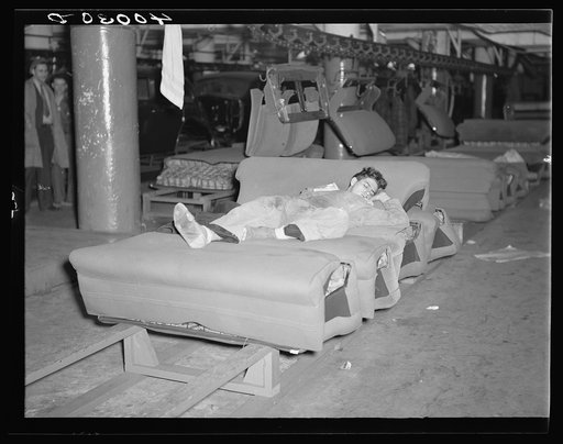 Young striker off sentry duty sleeping on assembly line of auto seats in Fisher body plant factory number three. Flint, Michigan