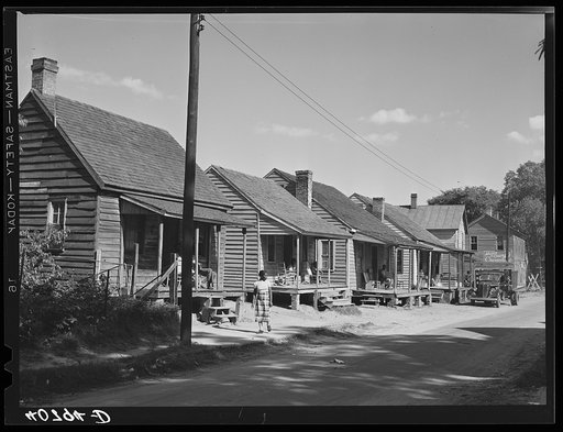 A street in the Negro quarter of Elizabeth City, North Carolina, where many of the migrants find lodging. In the background is one of the trucks that take them to and from work