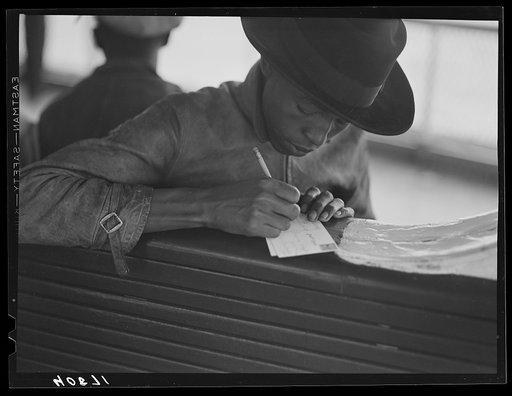Migratory worker on the Norfolk-Cape Charles Ferry, writing a postcard home to his parents