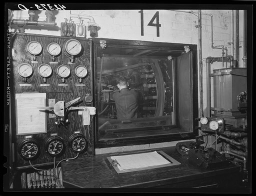 At the testing chamber for motors at the Pratt and Whitney Aircraft Corporation. After the engine is set up inside the chamber the door is sealed tight and the engine run at full blast for hours on end as an engineer watches it thru the window, records its performance as indicated by the instruments