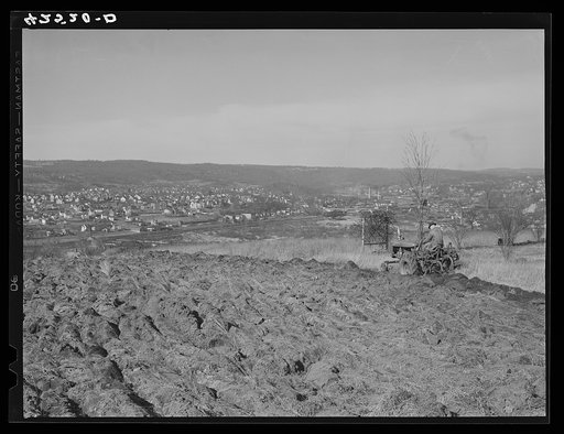 Farmer ploughing his field on a hillside opposite the industrial valley including the towns of Darby, Shelton, and Ansonia, Connecticut