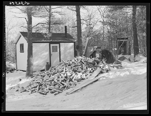 Mrs. M. Lane, young wife of a shipyard worker, gathering some wood just outside her one-room shack. The shack and little privy were built for them by her father. Made of celetex board. Bath, Maine