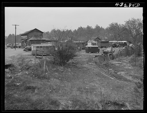 Part of a trailer camp for migratory workers, employed at Fort Bragg, North Carolina. Trailer space is one dollar a week, and small bunk houses five dollars a week. One water spigot near the general store serves the whole camp until 6 p.m. On the left is an old trolley car used as living quarters by