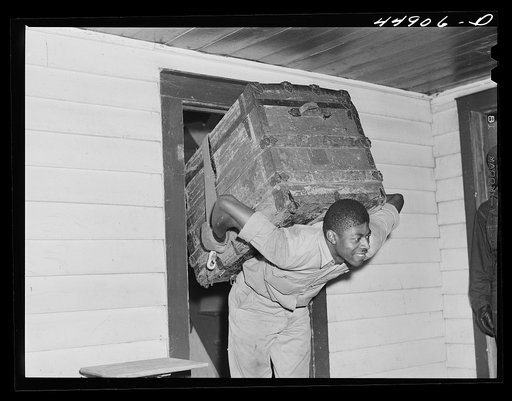 CCC (Civilian Conservation Corps) boy carrying a trunk out for a family who is moving out of the area taken over by the Army for maneuver grounds. Caroline County, Virginia