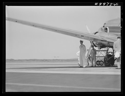 An airliner being readied for departure while another one is taking off in the background. Municipal airport, Washington, D.C.