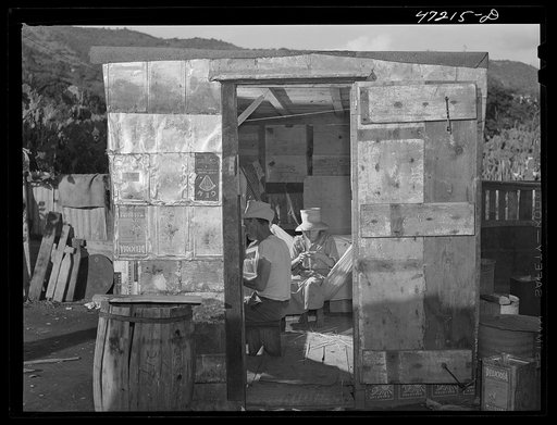 French village, a small settlement on Saint Thomas Island, Virgin Islands. A house in the French village, a small settlement, just outside Charlotte Amalie. This woman is weaving a hat of palm leaf, the man repairing a fish net