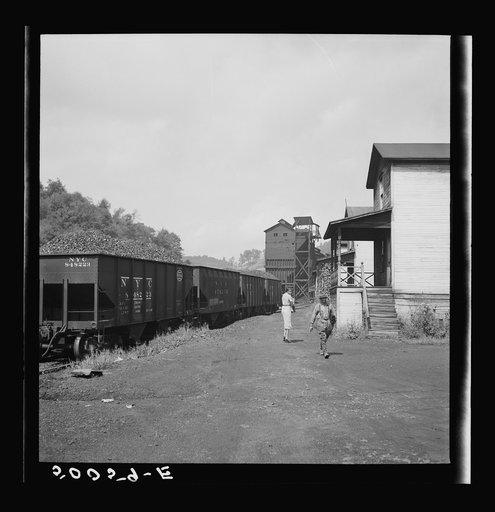 White coal miner going to work and Negro woman taking home groceries. Company houses, coal tipple in background. Pursglove, Scotts Run, West Virginia