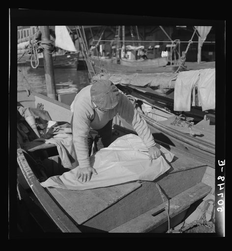 Untitled photo, possibly related to: Fisherman oiling waterproof jackets and pants in boat. Christmas Day, Charleston, South Carolina