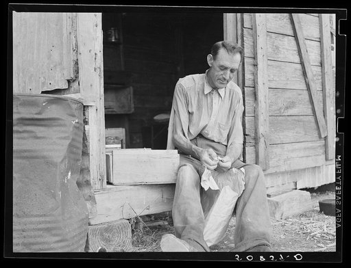 Former railroad worker shelling beans for his supper in front of his shack. He is now picking beans in Belle Glade, Florida