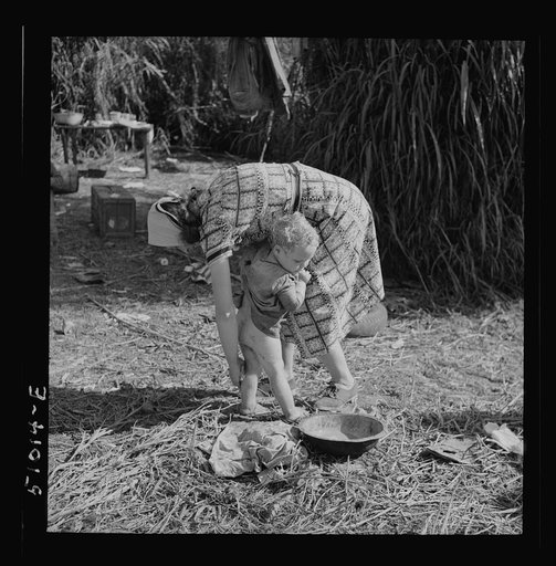 Woman packinghouse worker from Tennessee trying to wash black muck, which causes an itchy rash and sores, off her youngest child. She has three others. The water came from a filthy canal nearby. Belle Glade, Florida