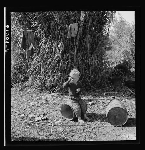 Child of packinghouse workers from Tennessee, his face covered with black muck which causes an itchy rash.  Belle Glade, Florida