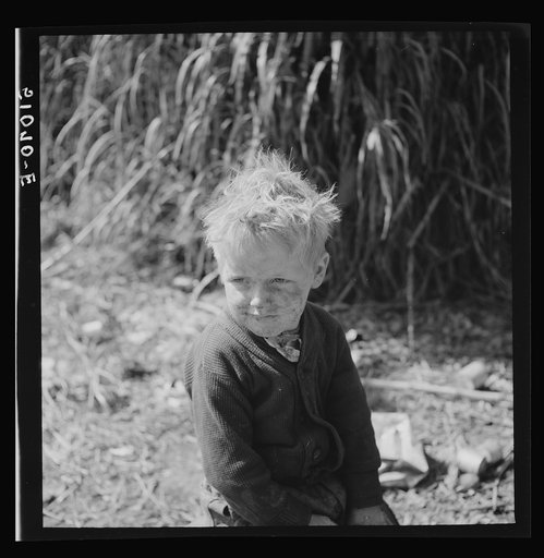 Child of packinghouse workers from Tennessee, his face covered with black muck which causes an itchy rash.  Belle Glade, Florida