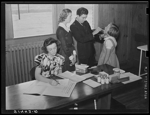 Nurse and doctor examining throat and teeth of child in health room of Goodman School with first grade teacher keeping records. Coffee County